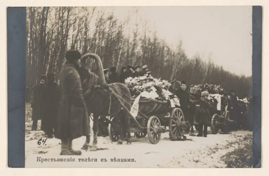 Крестьянская телега, заваленная цветами и венками с лентами, на заснеженной лесной дороге, рядом люди в тулупах
